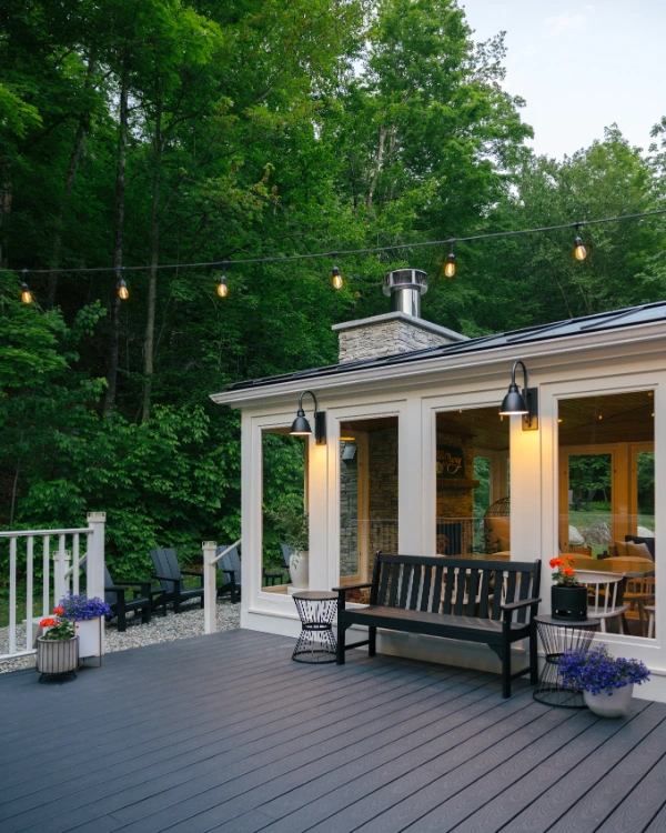 Covered outdoor seating area with bench and chairs overlooking the wooded yard